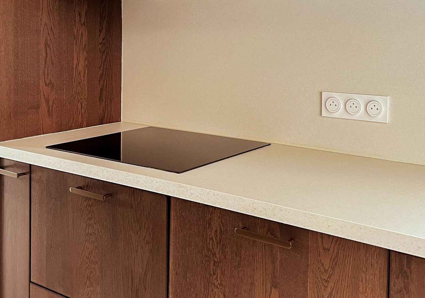 Cuisine minimaliste avec meubles en bois foncé, plan de travail clair et plaque de cuisson intégrée – réalisation Aesthetica Interiors