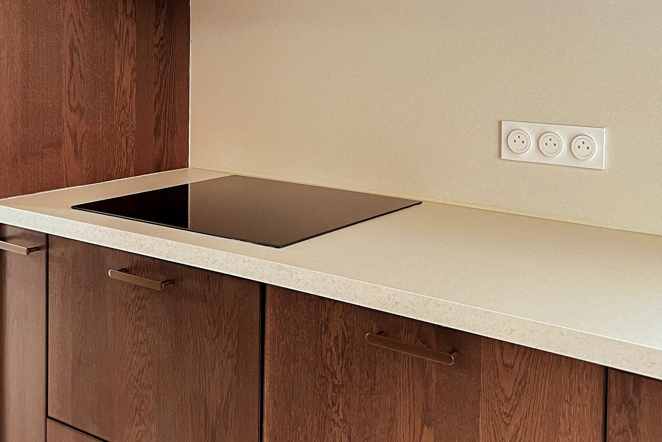 Cuisine minimaliste avec meubles en bois foncé, plan de travail clair et plaque de cuisson intégrée – réalisation Aesthetica Interiors